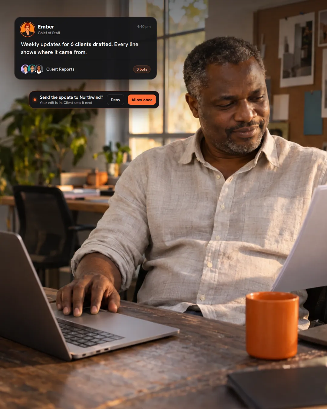 A small agency owner in his office reading a printed client report, while Ember, his AI Chief of Staff, reports six client updates drafted and waits for his yes before one goes to the client.