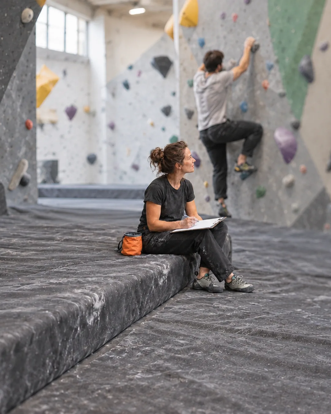 A climbing gym owner sits by the bouldering wall watching members, working out what keeps them coming back.