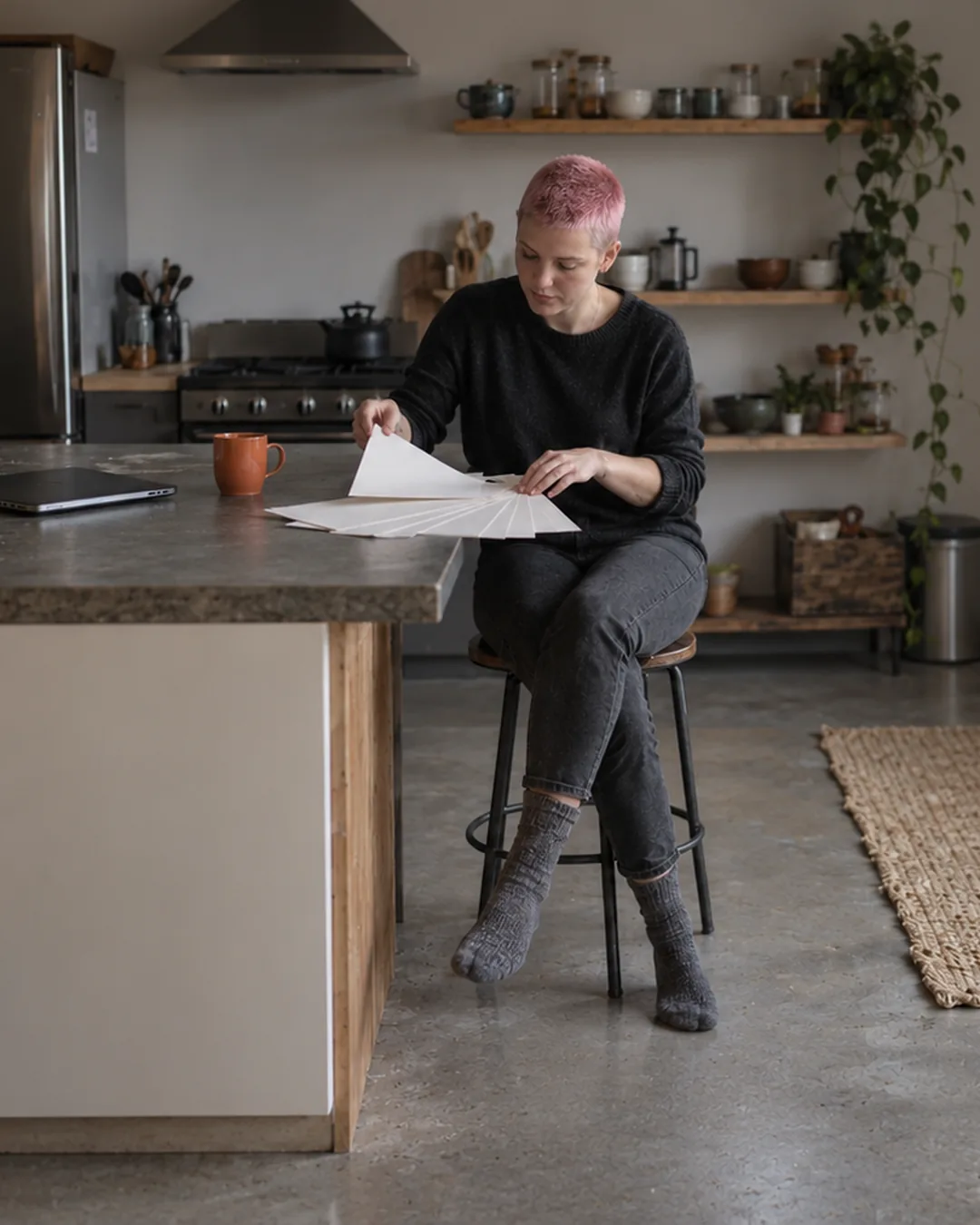 A designer fans out printed sample pages at her kitchen counter in soft overcast morning light.