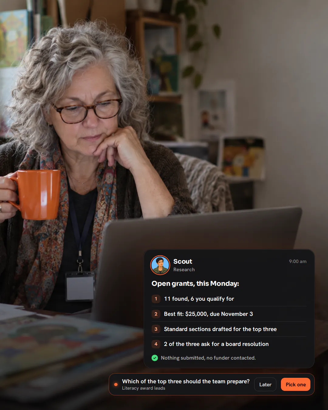 A nonprofit director at a desk surrounded by children’s books, reading her laptop with a mug on a Monday morning.