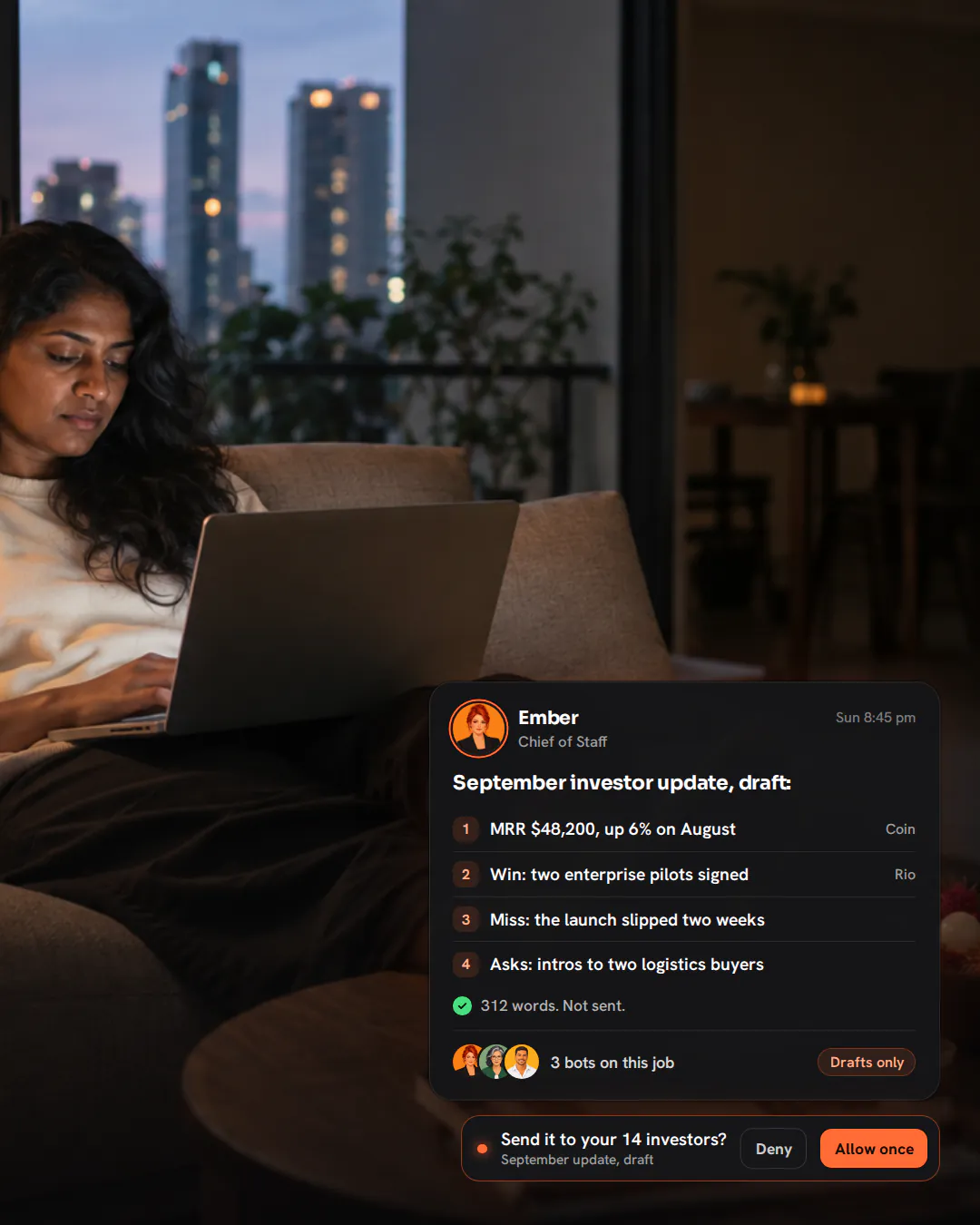 A startup founder on her sofa on a Sunday evening with a laptop on her knees, city towers at dusk behind her.