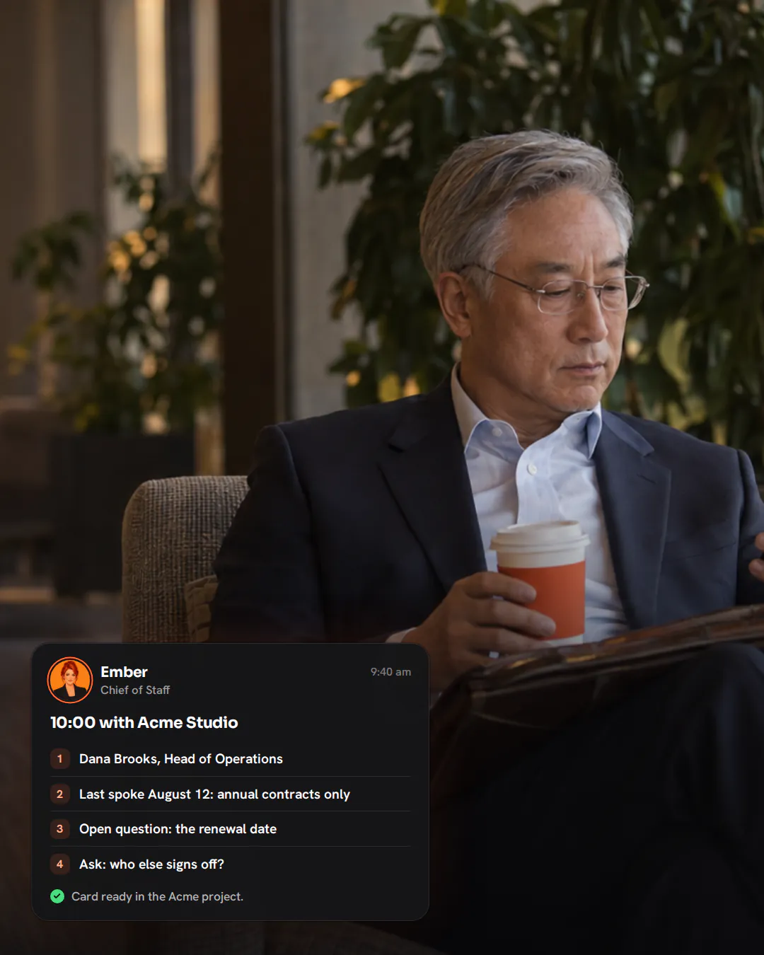 A real-estate broker in a suit sitting in a hotel lobby armchair with a coffee, reading his phone before a meeting.