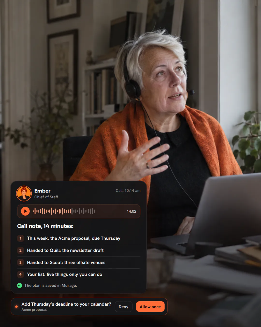 An interior designer with a headset leaning back at her desk by a window, talking and gesturing mid-sentence.